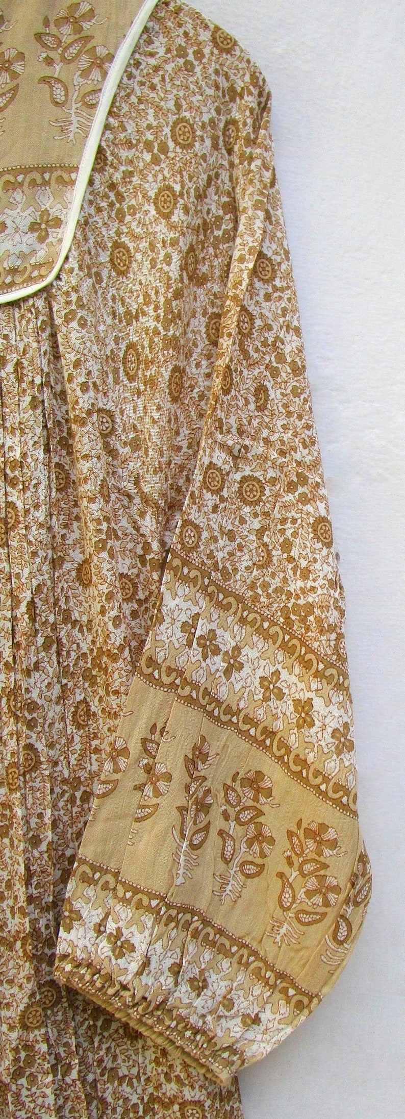 May include: A white cotton dress with a brown floral print. The dress has a white collar and long sleeves with a brown floral print border.