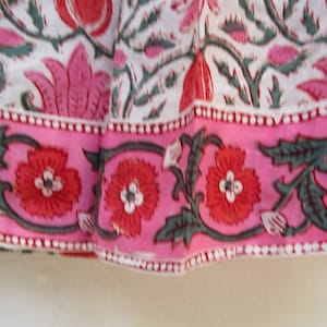 Puede incluir: Primer plano de una tela rosa y blanca con estampado floral. La tela tiene un borde rosa con un patr&oacute;n repetido de hojas verdes y flores rojas.