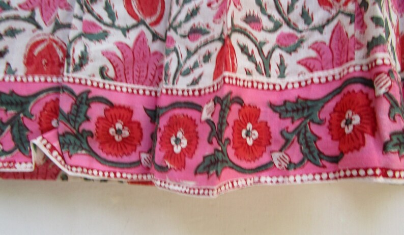 Puede incluir: Primer plano de una tela rosa y blanca con estampado floral. La tela tiene un borde rosa con un patr&oacute;n repetido de hojas verdes y flores rojas.
