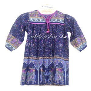 May include: A long-sleeved, navy blue tunic with a floral pattern and elephant design. The tunic has a V-neck with a drawstring and the text "nahata fashion shop". The sleeves are three-quarter length.