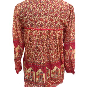 May include: A long-sleeved, red and cream colored tunic with an elephant print. The tunic has a V-neck and a gathered waist.
