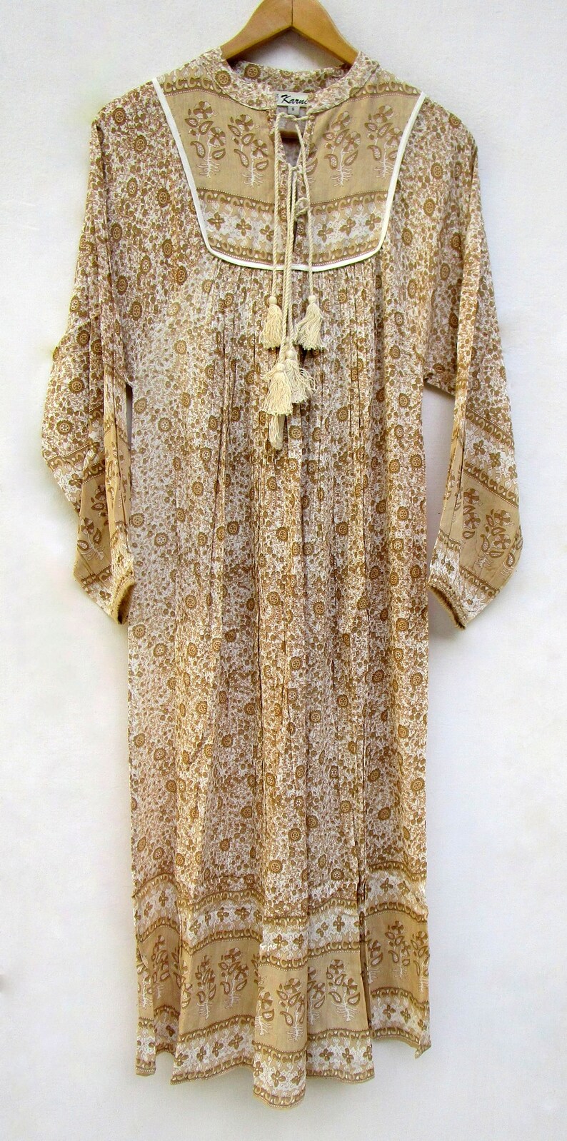May include: A long-sleeved, white and brown floral print dress with a white lace trim around the neckline. The dress has a tie at the neckline with tassels and a gathered skirt.