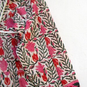 Puede incluir: Una blusa de algod&oacute;n blanco con estampado floral rosa y verde. La blusa tiene manga larga y un pu&ntilde;o fruncido. La tela es ligera y tiene una textura suave.