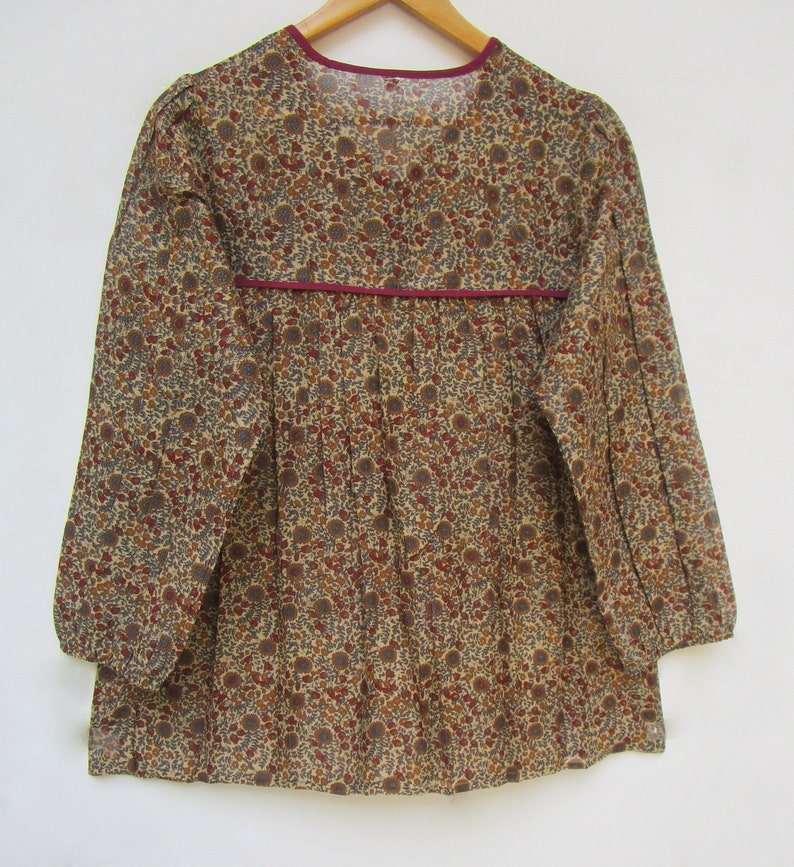 May include: A long-sleeved blouse with a floral pattern in shades of brown, red, and gray on a beige background. The blouse has a V-neckline and a burgundy trim along the neckline and waist. The sleeves are gathered at the cuffs.