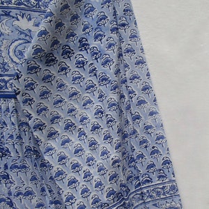 May include: A light blue and white patterned garment with a floral design. The fabric features a repeating pattern of blue flowers and a decorative border along the sleeve and neckline. The garment appears to be a long-sleeved top or dress.