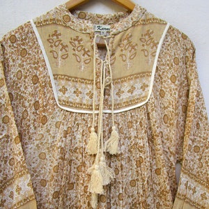 May include: A white and brown floral print cotton tunic top with a tie neckline and tassel details. The top has a white trim around the neckline and a small label that says "Karuni" on the front.