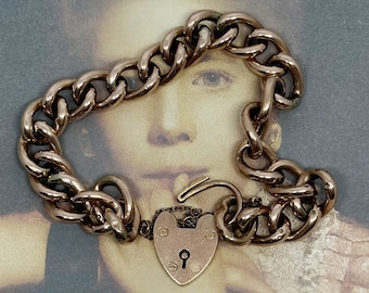 May include: A gold heart-shaped padlock charm bracelet with a curb chain. The bracelet is on a vintage photograph of a young girl.