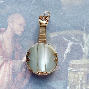 May include: A gold-toned pendant shaped like a banjo with a mother-of-pearl inlay. The pendant has a detailed design and is a unique piece of jewelry.