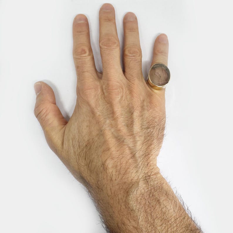 May include: A gold ring with a large, round, clear stone set in a bezel setting. The ring is on a person's finger.