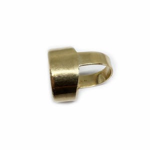 May include: A gold ring with a wide band and a unique open design. The ring is made of a smooth, polished metal.