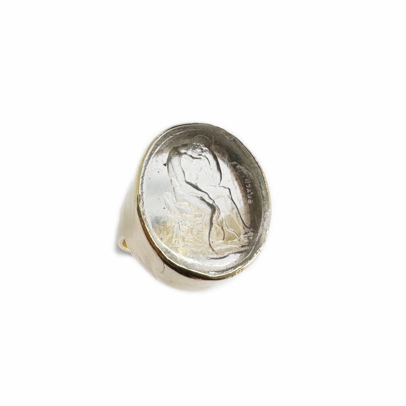May include: A silver ring with a clear glass inset featuring a profile of a woman's face. The glass is slightly cloudy and the woman's face is visible through the glass. The ring is set on a white background.
