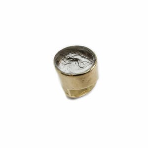 May include: A gold ring with a round, clear stone set in the top. The stone has a textured, silver-colored design.