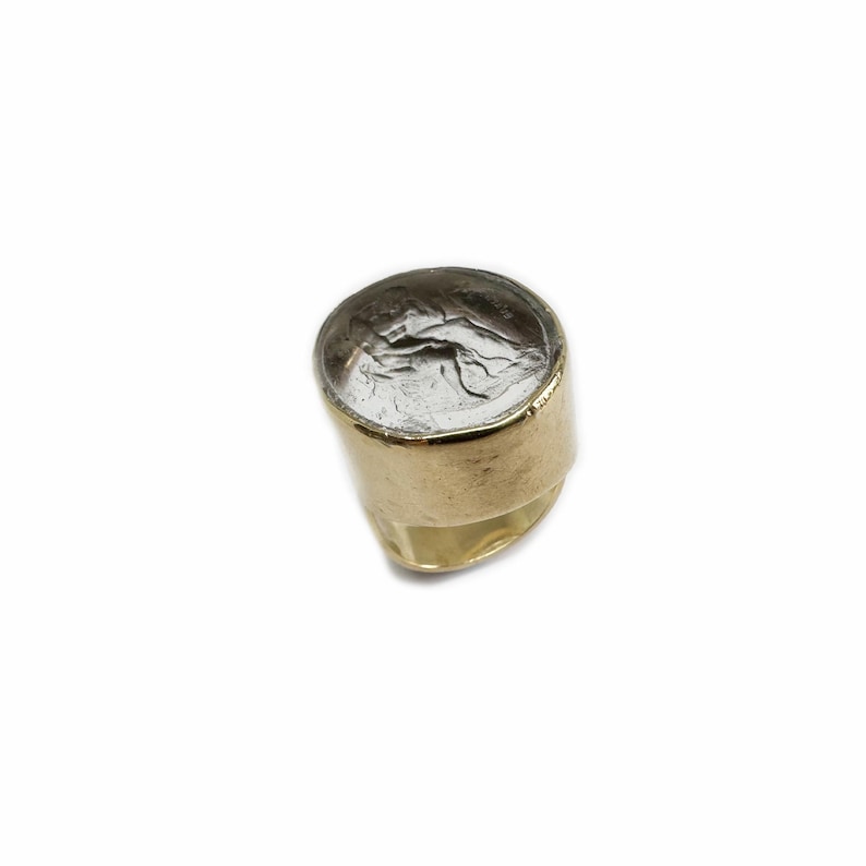 May include: A gold ring with a round, clear stone set in the top. The stone has a textured, silver-colored design.