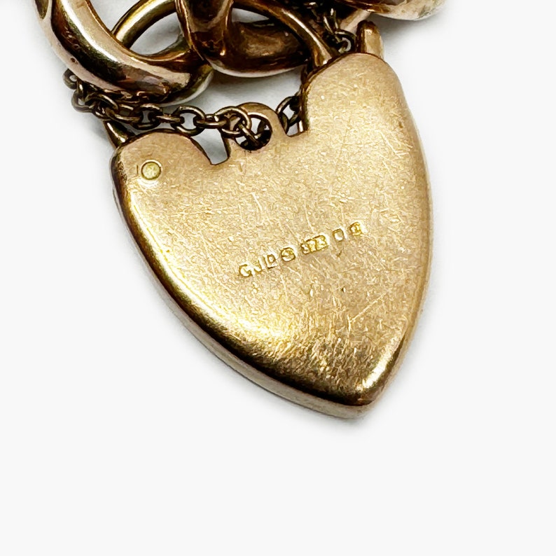 May include: Close-up of a gold heart-shaped charm with the inscription "9ct 375" on the back.