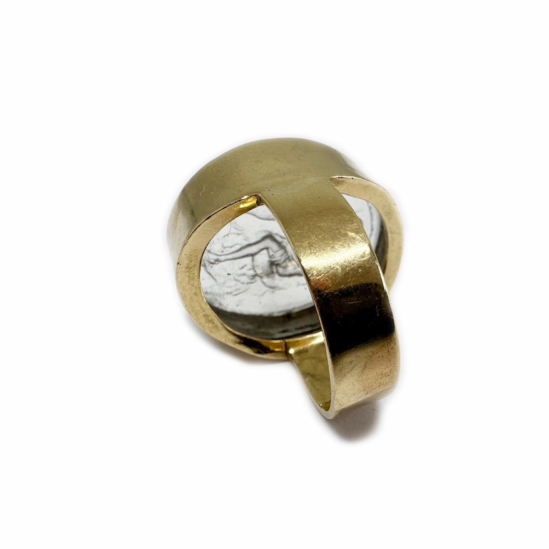 May include: A gold ring with a clear stone set in the center. The stone has a design etched into it.