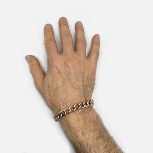 May include: A gold chain bracelet on a person's wrist.