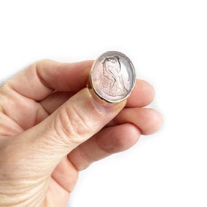 May include: A silver ring with a pink cameo featuring a sculpted image of two figures. The ring is set in a gold band.