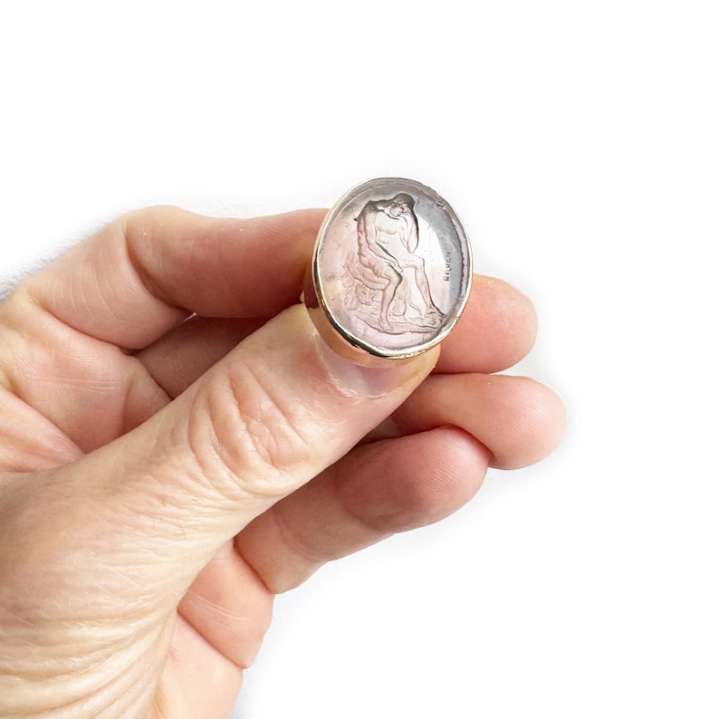 May include: A silver ring with a pink cameo featuring a sculpted image of two figures. The ring is set in a gold band.