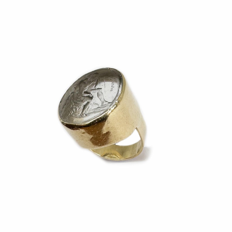 May include: A gold ring with a silver coin set into the top. The coin features a detailed image of a person and the word "ROMA".