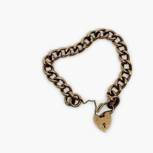 May include: A gold chain bracelet with a heart-shaped padlock clasp. The chain is a curb style and the padlock has a keyhole.