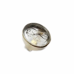 May include: A clear glass ring with a gold setting. The glass features a raised design of a figure.