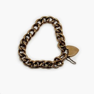May include: A gold chain bracelet with a heart-shaped charm. The chain is thick and has a curb link design.