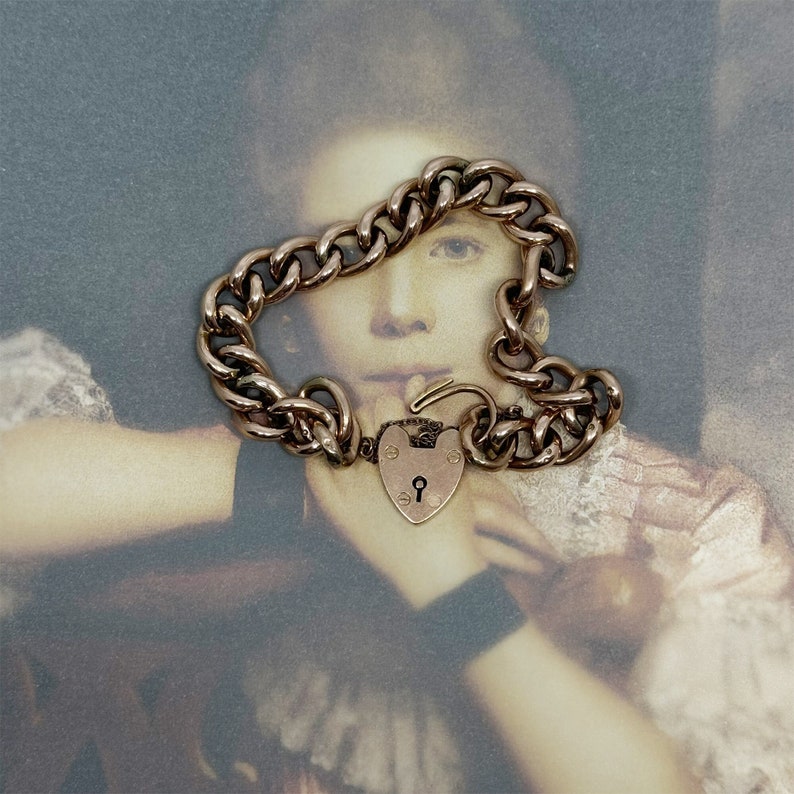 May include: A gold heart-shaped padlock charm bracelet with a curb chain. The bracelet is on a vintage photograph of a young girl.