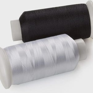 May include: Two cylindrical spools of sewing thread, one black and one white, each featuring a smooth plastic core with wide circular ends. The thread is tightly wound around the centre of each spool, creating a uniform and dense texture.