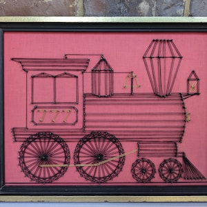 May include: A framed string art piece depicting a red train engine with the number 777 on the side. The train is outlined in black string and the background is a solid red.