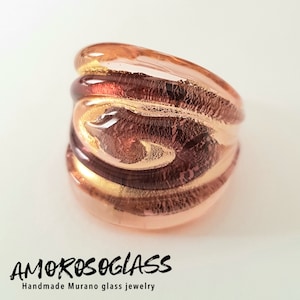 Può includere: Un anello in vetro rosa e marrone con accenti dorati. L'anello è fatto a mano e presenta un motivo a spirale.