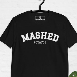 Puede incluir: Camiseta negra con texto blanco que dice "MASHED POTATOS" en una fuente de estilo universitario. La camiseta tiene un pequeño logotipo en la parte superior izquierda que dice "NINANUSH".