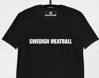 May include: Black t-shirt with the text "SWEDISH MEATBALL" in white, displayed prominently across the front. The shirt is hanging on a black hanger against a white brick wall. The brand logo is visible at the top.