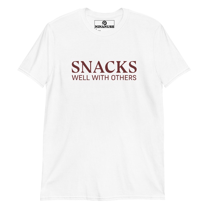 May include: White t-shirt with a maroon print that says "SNACKS WELL WITH OTHERS".