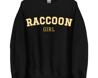Puede incluir: Sudadera negra con un gráfico amarillo "RACCOON GIRL" en una fuente universitaria.