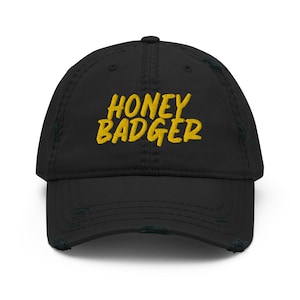 Könnte beinhalten: Schwarze Baseballkappe mit Distressed-Effekt und dem gelb gestickten Text "HONEY BADGER". Die Kappe hat einen gebogenen Schirm und einen abgenutzten, Vintage-Look.
