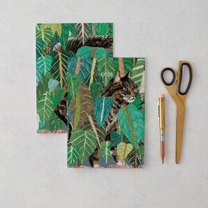 May include: Two green and brown illustrated notebooks with a cat and foliage design. The top notebook has the word "NOTES" printed on it.