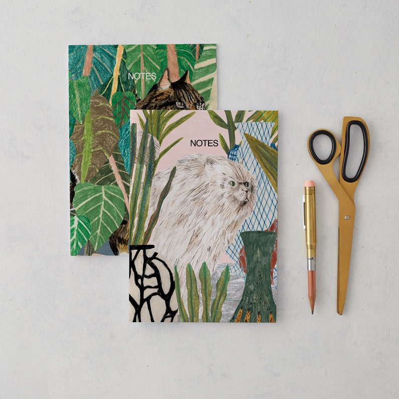 May include: Two notebooks with a tropical jungle theme. The top notebook features a cat with green leaves and the text "NOTES". The bottom notebook features a white cat with green leaves and the text "NOTES".