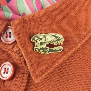 Tyrannosaurus Skull as a gold pin badge on orange jacket lapel. Design by James Barker