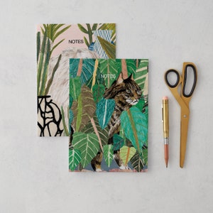 May include: Two notebooks with colorful illustrations. The top notebook has a pink background with green and blue plants and the text "NOTES". The bottom notebook has a green and blue background with a cat and the text "NOTES".