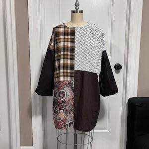 May include: A brown, black and white patchwork dress with a paisley print. The dress has a round neckline and long sleeves.