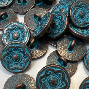 May include: A collection of teal blue and copper metal buttons with a decorative floral design. The buttons have a shank on the back for sewing.