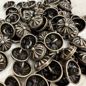 May include: A pile of antique gold-toned metal buttons with a cross design. The buttons have a raised cross design and a loop on the back for sewing.