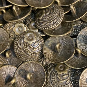 Pode incluir: Um monte de botões de metal dourado antigo com um design floral. Alguns botões têm uma superfície lisa, enquanto outros têm uma superfície texturizada.