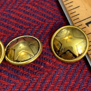 May include: Two gold-toned metal buttons with a star design. The buttons are round and have a raised star in the center.