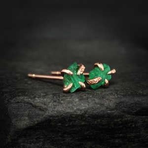 Puede incluir: Un par de pendientes de oro rosa con piedras preciosas de esmeralda en bruto. Las esmeraldas son de color verde oscuro y tienen una textura rugosa y natural. Los pendientes son simples y elegantes, perfectos para el uso diario.
