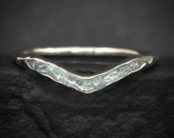 May include: A V-shaped ring featuring a series of small, light blue, textured stones set along the front curve of the polished silver-toned band. The design follows a chevron silhouette with a smooth, rounded finish on the back of the band.