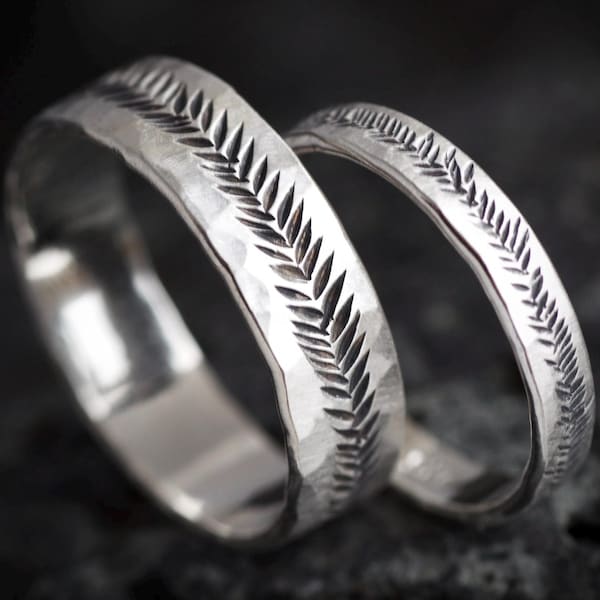 May include: Two silver rings with a hammered texture and a carved fern leaf pattern running along the outer surface. The rings feature a polished finish with darkened recessed areas within the leaf design, creating a high contrast appearance.