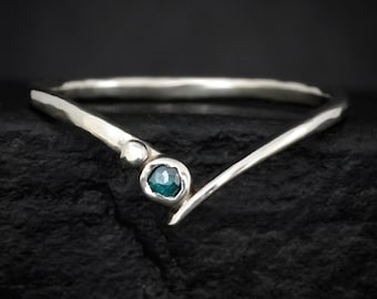 May include: A V-shaped silver ring featuring a hammered texture along the band. The ring is accented with a small, round, polished silver bead and a single, faceted, teal-coloured gemstone set in a circular bezel near the centre point.