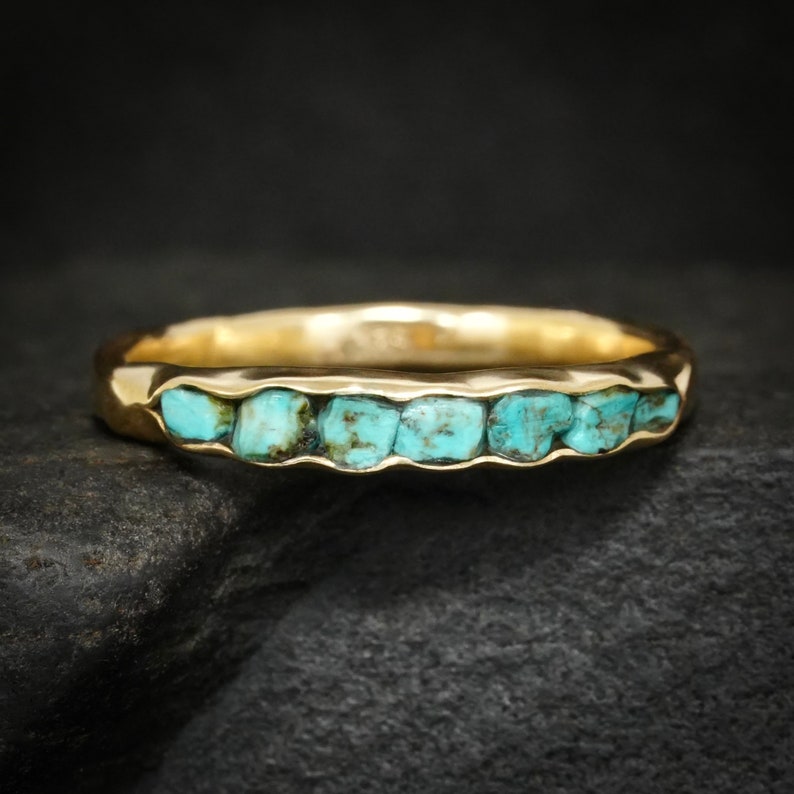 May include: A gold band ring with a row of turquoise stones set into the band.