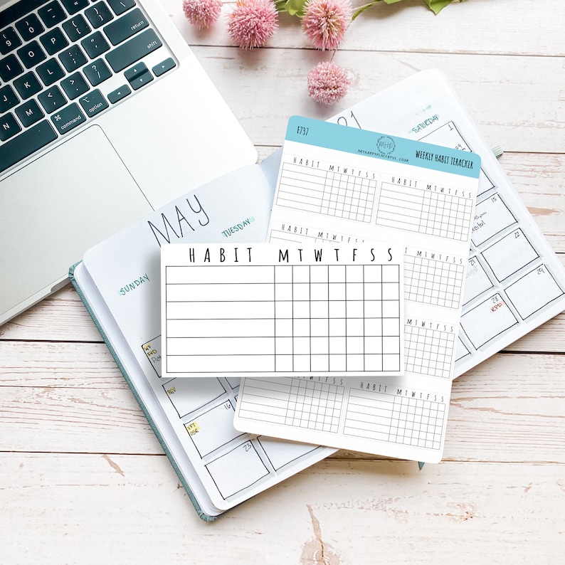 K&ouml;nnte beinhalten: Nahaufnahme eines wei&szlig;en Habit Trackers mit den Worten "HABIT" und "MTWTFSS" darauf gedruckt. Der Tracker liegt auf einem Planer mit dem Monat Mai und den Wochentagen darauf gedruckt.